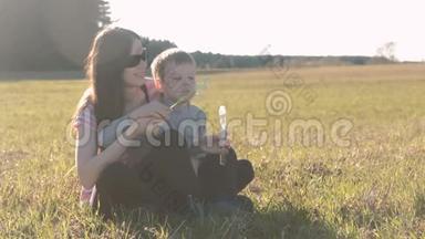 妈妈和儿子坐在草地上吹肥皂泡，全家周末在公园。