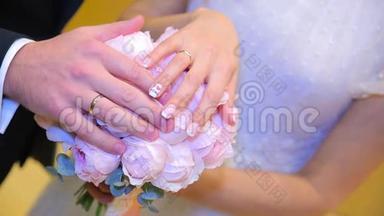 新婚夫妇`手里拿着结婚戒指。 新娘和新郎在鲜花或婚礼花束上戴着结婚戒指。 新婚夫妇