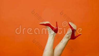 女人的腿`红色高跟鞋，背景是明亮的橙色。 它们从一侧摆动到另一侧。 红色专利鞋。 慢慢