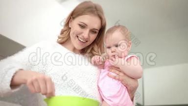 年轻的妈妈手里拿着婴儿做饭。 婴儿营养烹饪