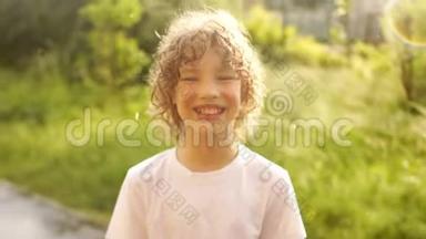 一个美丽的卷发男孩站在夏天温暖的雨下，微笑着。 儿童节。 节日快乐