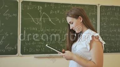 一个班上的女学生正在平板电脑上打字。 在有数学公式的学校董事会的背景下。