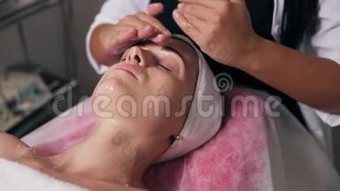 一位专业美容师的特写镜头`他在水疗沙龙做面部和<strong>颈部按摩</strong>。 年轻女子躺在床上