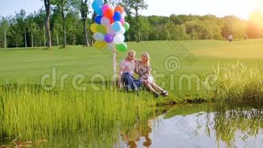 慢动作<strong>视频</strong>快乐的年轻夫妇坐在河岸上的<strong>气球</strong>