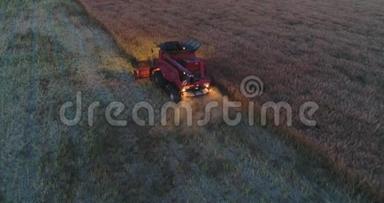 在日落时，在一片田野中的联合收割机上方的空中视野。 拖拉机和农用机械收获