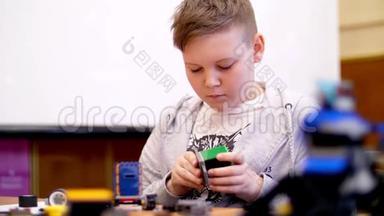这个11岁的男孩，从立方体、盘子、电路、电线中扮演设计师。 小发明家创造机器人