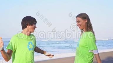 快乐的年轻志愿者穿着绿色t<strong>恤衫</strong>，在海滩上进行图像回收，向镜头致意