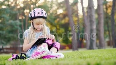 女孩坐在房子附近，享受着平板电脑。 在溜冰鞋上滚动-在她的头盔和滚轮上