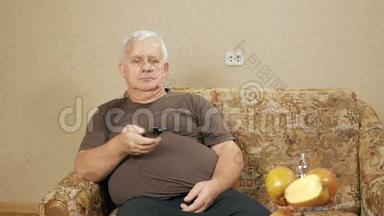 老人在家里的沙发上切换遥控电视频道。 经过一天的艰苦，他放松了。 假日家庭概念