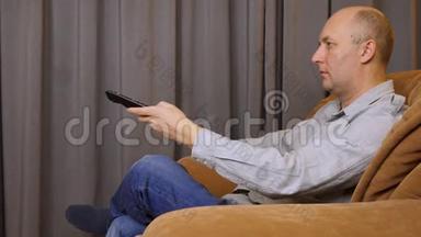 白人持有遥控器并将其用于媒体控制。 男子坐在扶手椅上，可选择使用遥控器