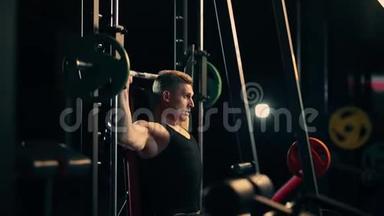 一个肌肉发达的人在一个黑暗的健身房里锻炼肩膀的肌肉，举重