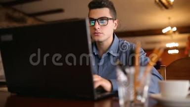 英俊的自由职<strong>业</strong>者商人戴眼镜，<strong>勤奋</strong>地在咖啡馆的笔记本电脑上工作。 男子键盘打字和搜索新