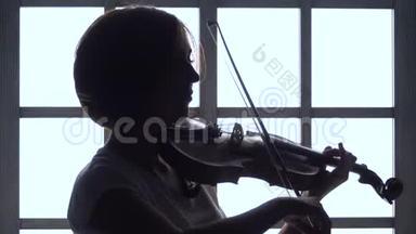 女孩用手指指着窗户拉小提琴。 剪影