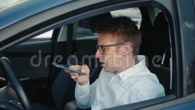 一个快乐的男人坐在车里，用智能手机语音识别功能在户外的一个背光公园里