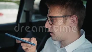 一个快乐的男人坐在车里，用智能<strong>手机</strong>语音识别<strong>功能</strong>在户外的一个背光公园里