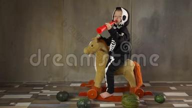 小男孩光着脚穿着<strong>骷髅</strong>服骑着摇摆玩具马。 儿童快乐庆祝<strong>万圣节</strong>，手持南瓜形手电筒