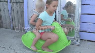 孩子们骑在绿色塑料马上，在<strong>农村房子</strong>的院子里的镜子背景上摇摆。 漂亮的孩子