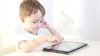 快乐的孩子坐在桌子旁，玩平板电脑。 孩子乐于玩电子游戏.. 儿童的概念