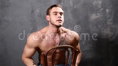 强壮和肌肉发达的人健美。 男人用椅子在黑色背景上摆姿势，显示他的肌肉。 漂亮的ABS和