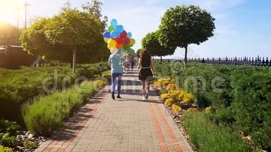 一对年轻夫妇带着一群五颜六色的<strong>气球</strong>在公园散步的慢动作<strong>视频</strong>