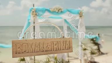 海滩上漂亮的婚礼拱门。 木制铭牌，上面有新娘和新郎的名字。 结婚纪念日。