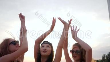女孩的双手在夕阳下，夏天，快乐的好朋友在沙滩上的夕阳下跳舞，女朋友举起手臂