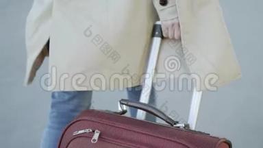 一个女人的手拿着把手提箱。 一个女人带着手提箱走到机场大楼。 一家企业