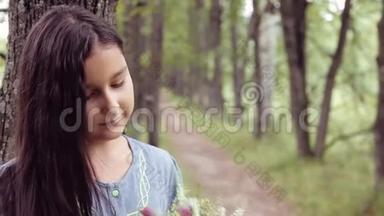 肖像。 一个甜美美丽的小女孩一边嗅着一束鲜花，一边幸福地看着相机微笑