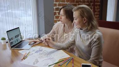 近距离拍摄<strong>创意</strong>时尚设计师的休闲<strong>服装</strong>，查看笔记本电脑和绘制草图。 两个女人