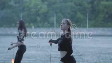 两个年轻女子站在河岸上表演火焰球。 熟练的火技艺术家表现出娴熟的技巧