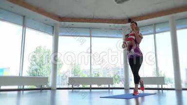 一个穿运动服的女人在瑜伽垫上蹲着，抱着她的婴儿在她的<strong>乳房</strong>上，慢动作