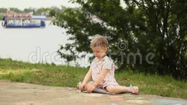 一个漂亮的小女孩在海滨长廊旁边的小径上画粉笔。
