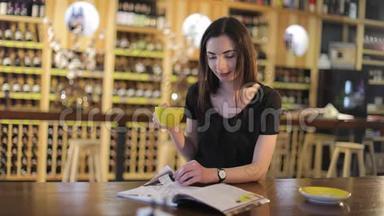 一个年轻的女孩喝咖啡，在咖啡馆或餐馆看时尚杂志，女人读杂志，喝酒