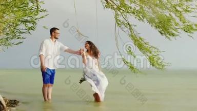 一个年轻人正把他的女孩摇在秋千上。 在雨中大海的背景下。 青年的浪漫与活力