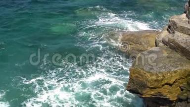 在晴朗晴朗的天气里，泡沫的波浪在岩石海岸上破浪前进