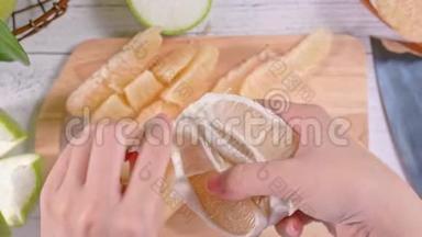 年轻的亚洲妇女正在剥鲜<strong>蜜柚</strong>，在明亮的白色木桌和砧板上的家庭厨房里吃，顶部的景色。