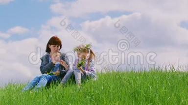 一个年轻的女人和她的女儿一起花圈。 坐在风景名胜区的草地上，靠着一片绿草