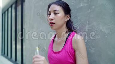慢动作-健康美丽的年轻亚洲跑步女子饮水，因为在城市街头跑步后感到疲倦。