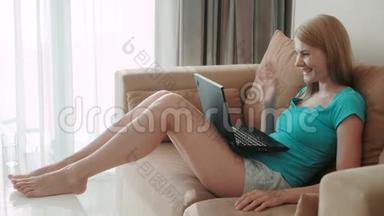 漂亮迷人的女人坐在沙发上拿着笔记本电脑。 通过电脑<strong>上网聊天</strong>