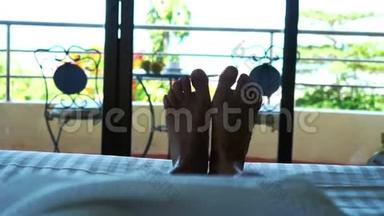 女人躺在酒店的床上，挥舞着她的脚对着热带海景。 3840x2160