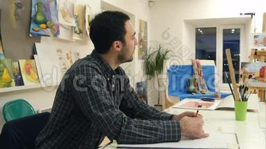 男艺术系学生用铅笔在画室的书桌前做素描