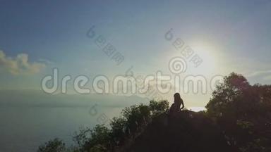 无人机表演女孩在清晨的阳光下在悬崖上放松
