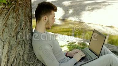 一个人坐在公园的树下，拿着笔记本电脑工作