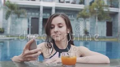 年轻的女人在泳池里用可尾音乐听着来自smarthone的耳机。