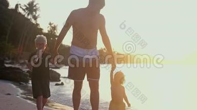快乐的父亲牵着孩子们`手，在美丽的夕阳下在热带海滩上散步。 旅游度假概念。 慢慢慢慢