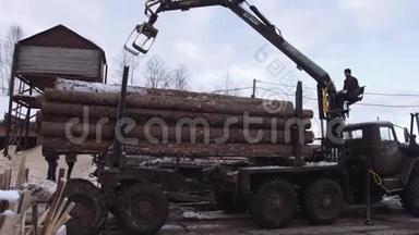 在锯木厂，机械铲装机从重型卡车上卸下木材原木