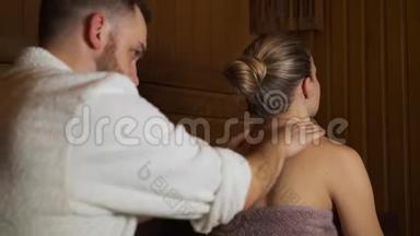 男人在桑拿、沐浴中做背部和颈部按摩美女。