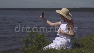 戴草帽的女孩在手机上拍照。 美丽的年轻女子在河边拍照