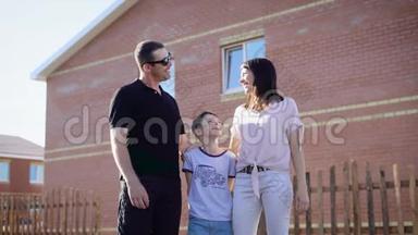 幸福的三口之家站在房子前面。 妈妈，爸爸和男孩。