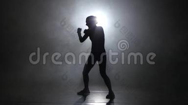 冠军拳手发<strong>出拳</strong>打脚踢。 剪影。 后方有灯光。 黑色背景。 侧视图
